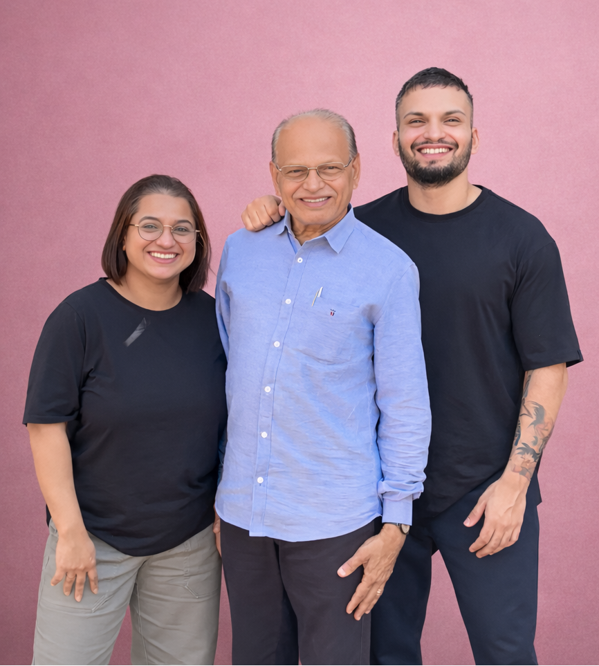 Shamien Menezes and Sheldon Menezes, co-founders of Super Munchies, with their father Robert Menezes, director, standing together against a pink background